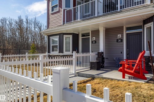 Front exterior of a multi-level residence featuring a white picket fence, a covered porch, and individual entry doors - 33 150 Everitt Dr, St. Albert, AB - Outdoor With Deck Patio Veranda
