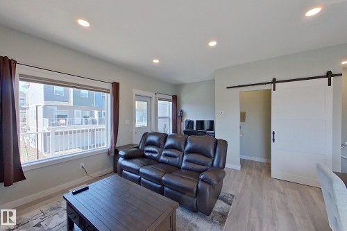 Living area featuring recessed lighting, a large window, light-toned wall paint, wood-finish flooring, and a white barn door with black hardware - 33 150 Everitt Dr, St. Albert, AB - Indoor Photo Showing Living Room