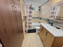 Bathroom featuring a light wood-finish vanity with a white countertop and integrated sink, a full bathtub with a shower, and tiled walls with an accent mosaic band - 