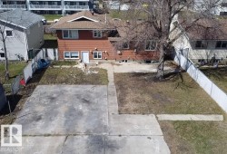 This property features a two-story residence with a brown siding facade, a front yard with a concrete pad, and a white shed - 