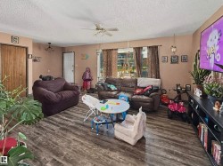Spacious living area featuring wood-finish flooring, abundant natural light from multiple windows, and a ceiling fan fixture - 