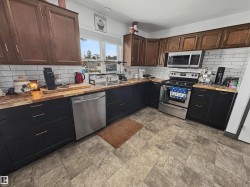 Spacious kitchen featuring wood-finish countertops, stainless steel appliances, a subway tile backsplash, and a double basin sink with a window view - 