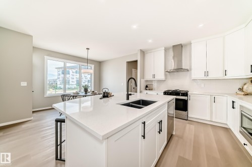 Modern kitchen featuring a central island with an undermount sink and matte black faucet, surrounded by white cabinetry with dark hardware - 1603 206 Street, Edmonton, AB - Indoor Photo Showing Kitchen With Double Sink With Upgraded Kitchen