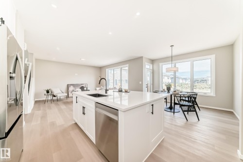 Open-concept living space featuring a white kitchen island with an integrated sink and dishwasher, stainless steel appliances, wood-finish flooring, recessed lighting, and multiple large windows - 1603 206 Street, Edmonton, AB - Indoor
