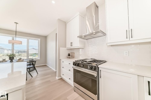 Modern kitchen featuring white cabinetry, stainless steel range with overhead vent hood, white subway tile backsplash, and light wood-finish flooring - 1603 206 Street, Edmonton, AB - Indoor Photo Showing Kitchen With Upgraded Kitchen