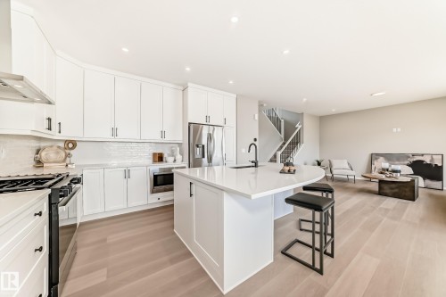 Modern kitchen featuring a white curved island with seating, white shaker-style cabinetry, and stainless steel appliances - 1603 206 Street, Edmonton, AB - Indoor Photo Showing Kitchen With Stainless Steel Kitchen With Upgraded Kitchen