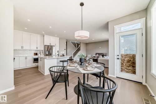 Open-concept dining area featuring light wood-finish flooring, a modern drum pendant light, and a white framed glass-paned door - 1603 206 Street, Edmonton, AB - Indoor