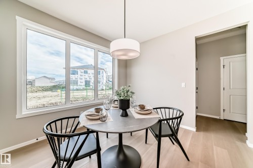 Bright dining area featuring a large picture window, a modern drum pendant light fixture, light wood-finish flooring, and neutral wall tones - 1603 206 Street, Edmonton, AB - Indoor Photo Showing Dining Room