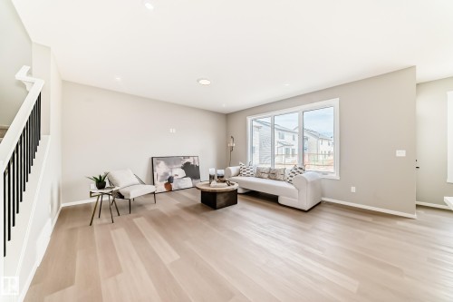 Spacious living area featuring light wood-finish flooring, a contemporary staircase with black metal balusters, recessed lighting, and large multi-pane windows providing ample natural light - 1603 206 Street, Edmonton, AB - Indoor