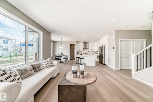 Expansive open-concept living area featuring large windows, light wood-finish flooring, a contemporary kitchen with white cabinetry and stainless steel appliances, and a dining area with modern pendant lighting - 1603 206 Street, Edmonton, AB - Indoor Photo Showing Living Room
