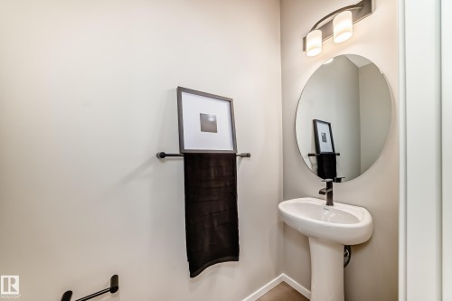 Pedestal sink with matte black faucet, round mirror, and modern wall-mounted light fixture - 1603 206 Street, Edmonton, AB - Indoor Photo Showing Bathroom