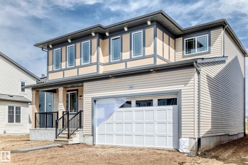 Contemporary two-story exterior featuring a single-car garage, covered entry porch with black railings, beige siding, and upper-level stucco detailing - 1603 206 Street, Edmonton, AB - Outdoor