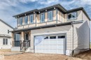 Contemporary two-story exterior featuring a single-car garage, covered entry porch with black railings, beige siding, and upper-level stucco detailing - 1603 206 Street, Edmonton, AB  - Outdoor 