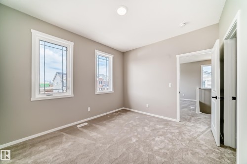 Neutral-toned room featuring two framed windows with white trim, light-colored carpeting, a white ceiling, and a white interior door with black hardware - 1603 206 Street, Edmonton, AB - Indoor Photo Showing Other Room