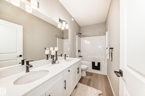 Bathroom featuring a dual vanity with white cabinetry and integrated sinks, matte black hardware, a combined shower and bathtub, and wood-finish flooring - 1603 206 Street, Edmonton, AB - Indoor Photo Showing Bathroom