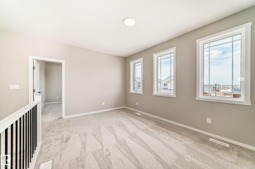 Carpeted bonus room featuring an angled ceiling, three large windows with white trim, and a contemporary black metal and white wood railing - 1603 206 Street, Edmonton, AB - Indoor Photo Showing Other Room