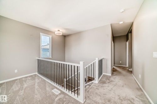 Carpeted landing area featuring a contemporary light fixture, a window with white trim, and a staircase with white newel posts and black metal balusters - 1603 206 Street, Edmonton, AB - Indoor Photo Showing Other Room