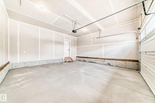 Spacious interior garage featuring a concrete floor, unpainted drywall walls, a white overhead door, and an interior access door with wooden steps - 1603 206 Street, Edmonton, AB - Indoor Photo Showing Garage