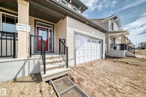 Contemporary home exterior featuring neutral siding, a red entry door with sidelights, and a white panel garage door - 1603 206 Street, Edmonton, AB - Outdoor