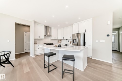 Modern kitchen featuring white cabinetry, light wood-finish flooring, a stainless steel refrigerator, and a kitchen island with seating - 1603 206 Street, Edmonton, AB - Indoor Photo Showing Kitchen With Stainless Steel Kitchen With Upgraded Kitchen