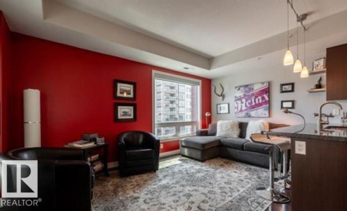 Living area featuring an accent wall, large window with city views, wood-finish flooring, recessed lighting, and a kitchen island with pendant lights - 702 10055 118 Street, Edmonton, AB - Indoor Photo Showing Other Room