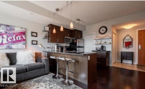 Open-concept living space featuring wood-finish flooring, a kitchen island with granite countertop, dark wood cabinetry, and stainless steel appliances - 702 10055 118 Street, Edmonton, AB - Indoor Photo Showing Kitchen