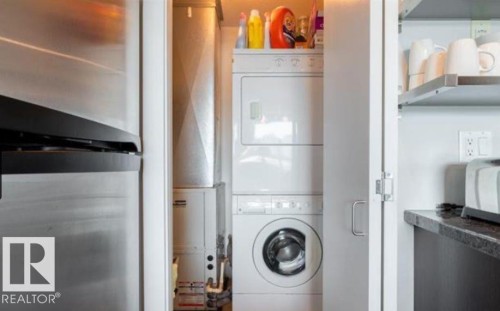 Integrated laundry closet featuring a stackable washer and dryer, adjacent to a stainless steel refrigerator - 702 10055 118 Street, Edmonton, AB - Indoor Photo Showing Laundry Room