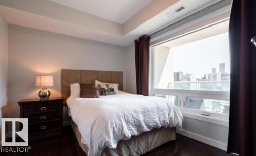 Expansive window framing city architecture, complemented by rich dark wood-finish flooring - 702 10055 118 Street, Edmonton, AB - Indoor Photo Showing Bedroom