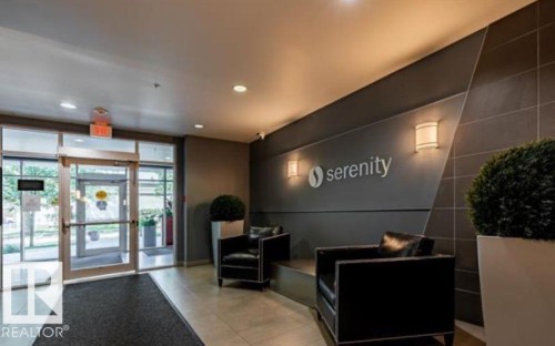 Contemporary lobby featuring a glass entry system, recessed lighting, wall sconces, and a dark accent wall with decorative paneling - 702 10055 118 Street, Edmonton, AB - Indoor Photo Showing Other Room