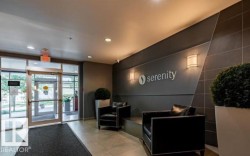 Contemporary lobby featuring a glass entry system, recessed lighting, wall sconces, and a dark accent wall with decorative paneling - 