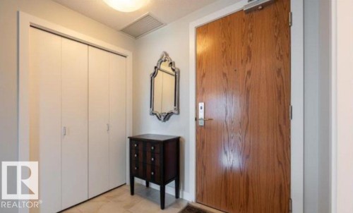 Entryway featuring a wood-grain door with modern hardware, bi-fold closet doors, and light-toned floor tiling - 702 10055 118 Street, Edmonton, AB - Indoor Photo Showing Other Room