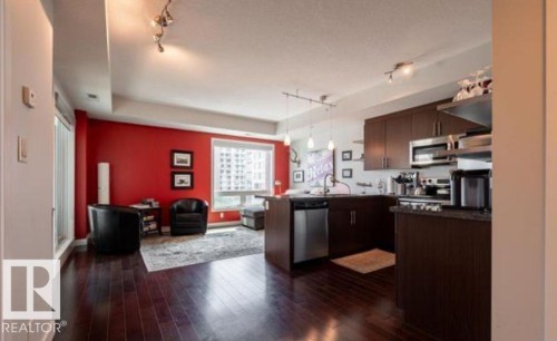 Open-concept living area featuring rich dark wood-finish flooring, a contemporary kitchen with dark cabinetry, stainless steel appliances, and a peninsula island with pendant lighting - 702 10055 118 Street, Edmonton, AB - Indoor Photo Showing Kitchen