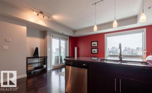 Kitchen island featuring a dark countertop, undermount sink, gooseneck faucet, and integrated stainless steel dishwasher - 702 10055 118 Street, Edmonton, AB - Indoor Photo Showing Kitchen
