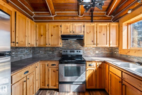 Kitchen featuring abundant natural wood cabinetry, stainless steel appliances, a mosaic tile backsplash, and dark countertops - A & B, 4858 Centre St, New Sarepta, AB - Indoor Photo Showing Kitchen