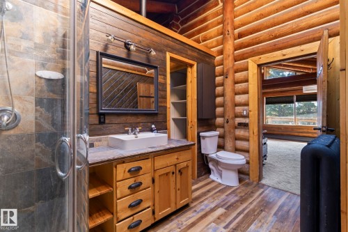 Bathroom featuring a glass-enclosed shower with natural stone-finish tile, a wood vanity with a vessel sink and stone-finish countertop, plank wood-finish flooring, and log wall accents - A & B, 4858 Centre St, New Sarepta, AB - Indoor Photo Showing Bathroom