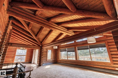 Expansive room featuring log construction, exposed timber beams, a wood-plank ceiling, multiple windows, and carpet flooring - A & B, 4858 Centre St, New Sarepta, AB - Indoor Photo Showing Other Room