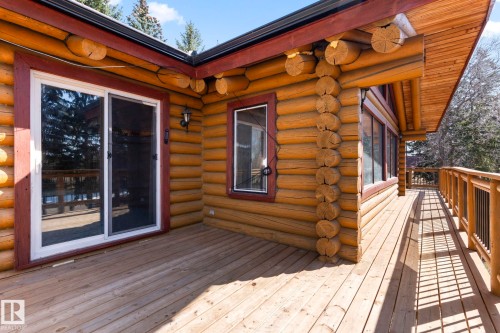 Expansive wood deck with natural wood railing, featuring a log cabin exterior, multiple windows, and a sliding glass door - A & B, 4858 Centre St, New Sarepta, AB - Outdoor With Deck Patio Veranda With Exterior