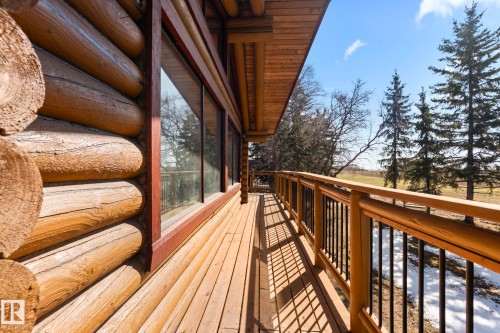 Exterior log construction featuring a wooden balcony with black metal balusters, large windows, and a natural tree-lined backdrop - A & B, 4858 Centre St, New Sarepta, AB - Outdoor With Deck Patio Veranda With Exterior