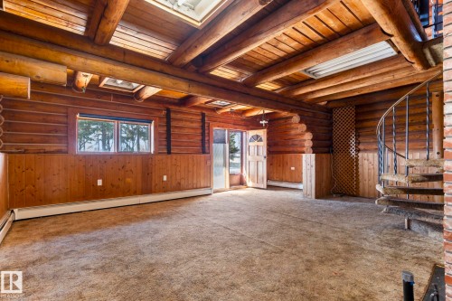 Spacious room featuring log construction walls, exposed timber ceiling beams, skylights, a spiral staircase with wrought iron balusters, and a window providing natural light - A & B, 4858 Centre St, New Sarepta, AB - Indoor Photo Showing Other Room