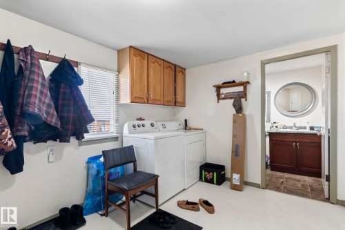 Dedicated laundry space featuring overhead wood cabinetry, a window with blinds, and light-toned flooring - A & B, 4858 Centre St, New Sarepta, AB - Indoor Photo Showing Laundry Room