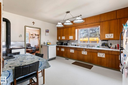 Kitchen featuring wood cabinetry, a double basin sink, white tile backsplash, and light-toned flooring - A & B, 4858 Centre St, New Sarepta, AB - Indoor Photo Showing Kitchen With Double Sink