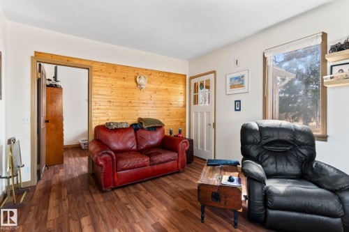 Interior room featuring wood-finish flooring, a natural wood paneled accent wall, white painted walls, and a white paneled door with window inserts - A & B, 4858 Centre St, New Sarepta, AB - Indoor Photo Showing Living Room