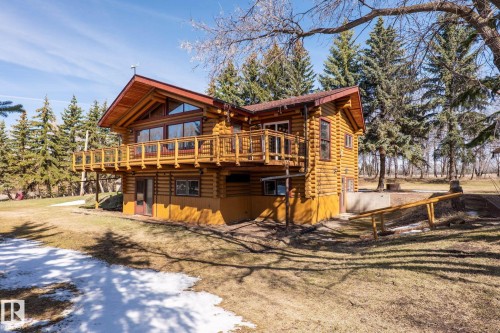 Rustic log home featuring a spacious exterior balcony, A-frame window design, prominent gabled roof, natural wood construction, and surrounding mature evergreen trees - A & B, 4858 Centre St, New Sarepta, AB - Outdoor With Deck Patio Veranda