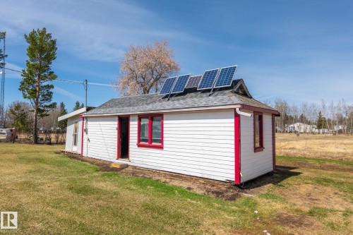 Compact structure featuring white siding with red trim, a dark shingle roof, and roof-mounted solar panels - A & B, 4858 Centre St, New Sarepta, AB - Outdoor
