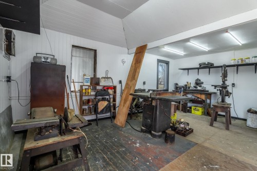 Spacious workshop with exposed wood-finish flooring, white paneling, multiple windows, built-in shelving, and overhead fluorescent lighting - A & B, 4858 Centre St, New Sarepta, AB - Indoor Photo Showing Other Room