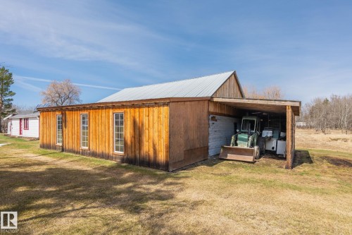 Wooden outbuilding with a galvanized metal roof, featuring multiple vertical windows and an integrated open-sided storage area - A & B, 4858 Centre St, New Sarepta, AB - Outdoor