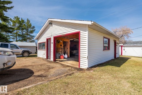 Detached garage structure featuring white siding, red trim, and an attached carport - A & B, 4858 Centre St, New Sarepta, AB - Outdoor With Exterior