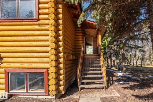 Log cabin exterior featuring a prominent log construction, red-framed windows, an exterior wood staircase with railings, a covered entryway, and surrounding mature trees - A & B, 4858 Centre St, New Sarepta, AB - Indoor Photo Showing Other Room