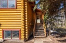 Log cabin exterior featuring a prominent log construction, red-framed windows, an exterior wood staircase with railings, a covered entryway, and surrounding mature trees - A & B, 4858 Centre St, New Sarepta, AB  - Indoor Photo Showing Other Room 