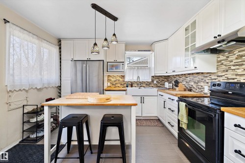 Kitchen featuring white cabinetry, butcher block countertops, a farmhouse sink, stainless steel refrigerator, and a mosaic tile backsplash - 11607 141 Street, Edmonton, AB - Indoor Photo Showing Kitchen With Upgraded Kitchen